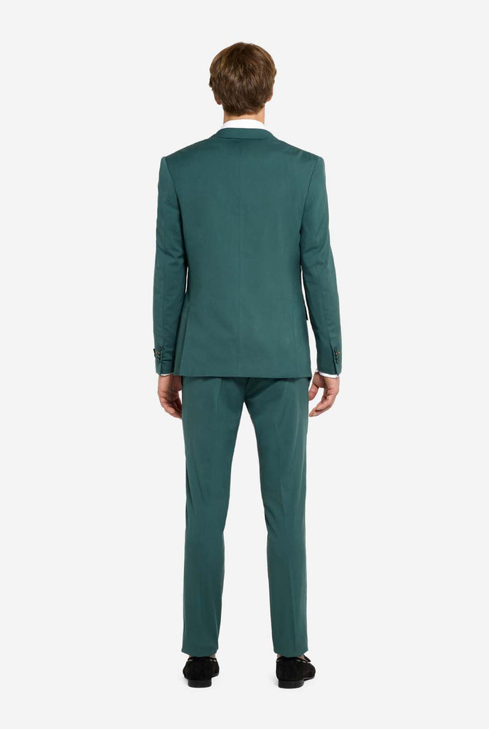 Image with light grey background and man wearing dark green men’s suit and white shirt. Suits consists of blazer and pants. Man facing away from the camera and showing the back of the suit. 